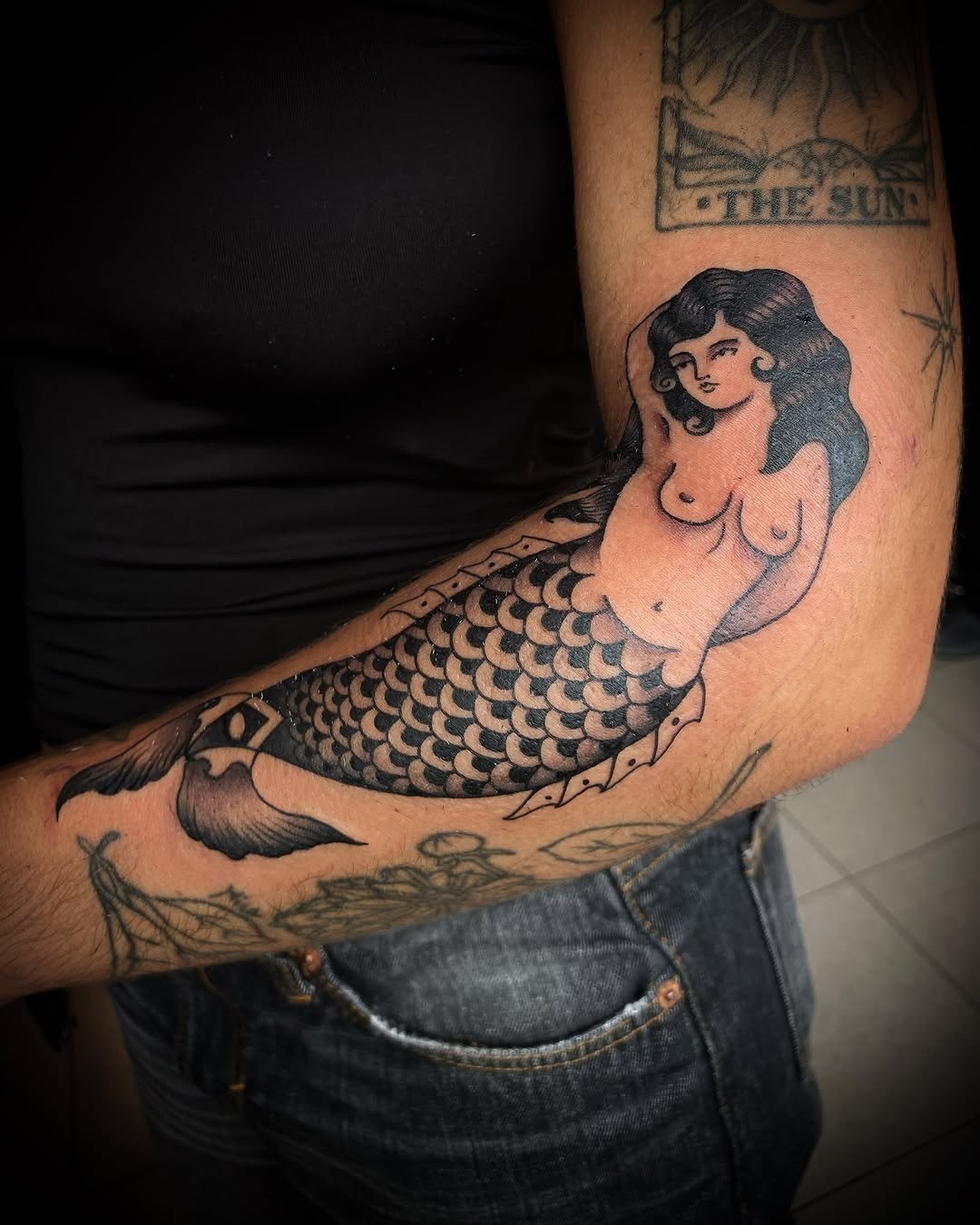 Sereia a preto e cinzento tatuada num braço