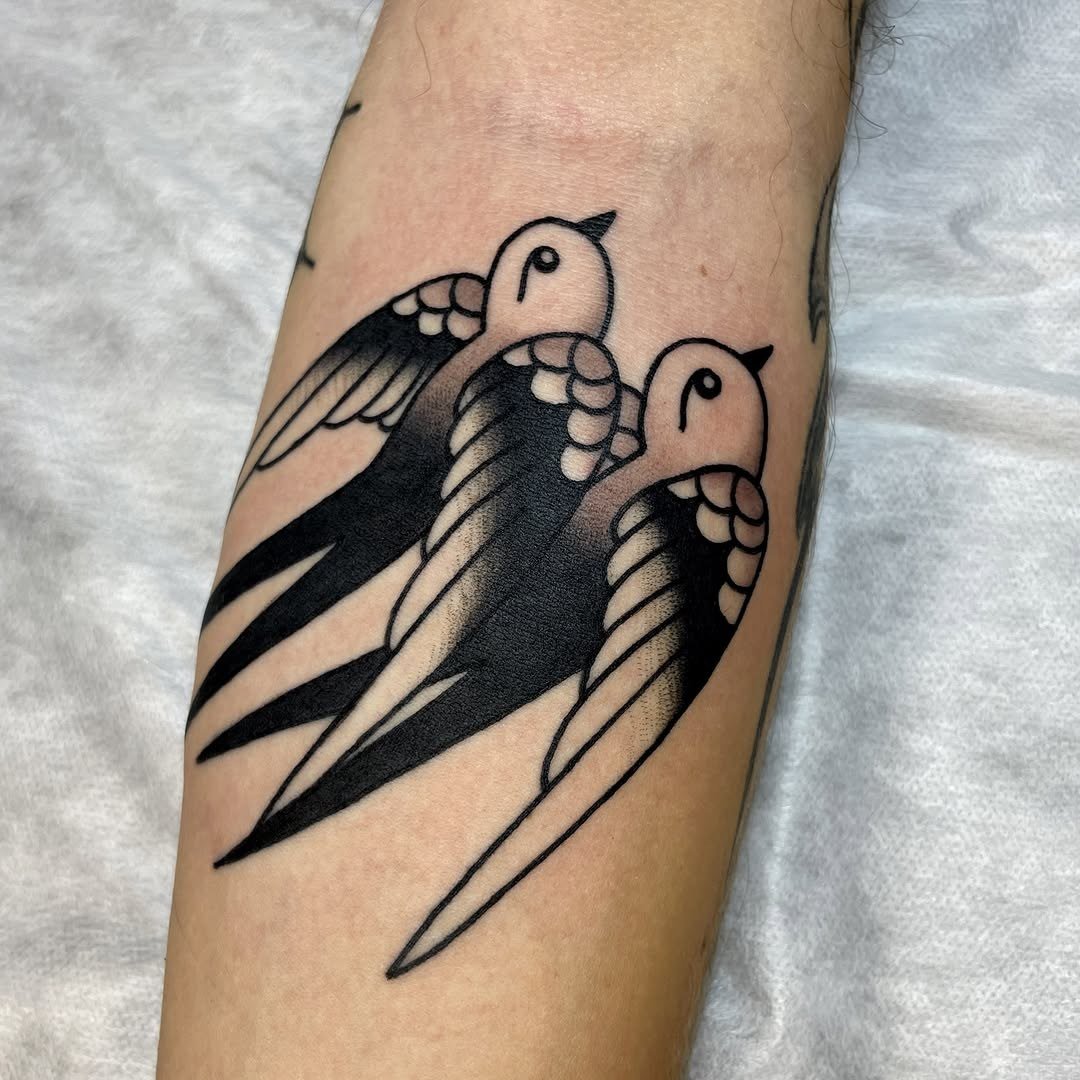 Tatuagem de três andorinhas a preto num antebraço